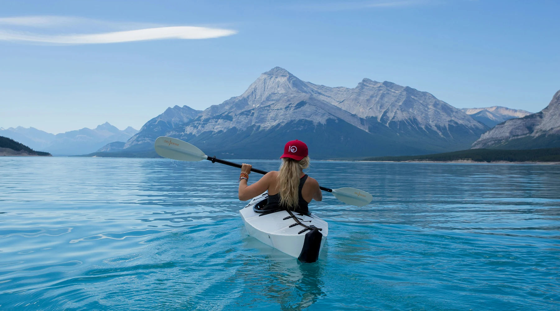 A person kayaking on a pristine mountain lake with clear blue water, surrounded by towering mountain peaks under a clear sky.
