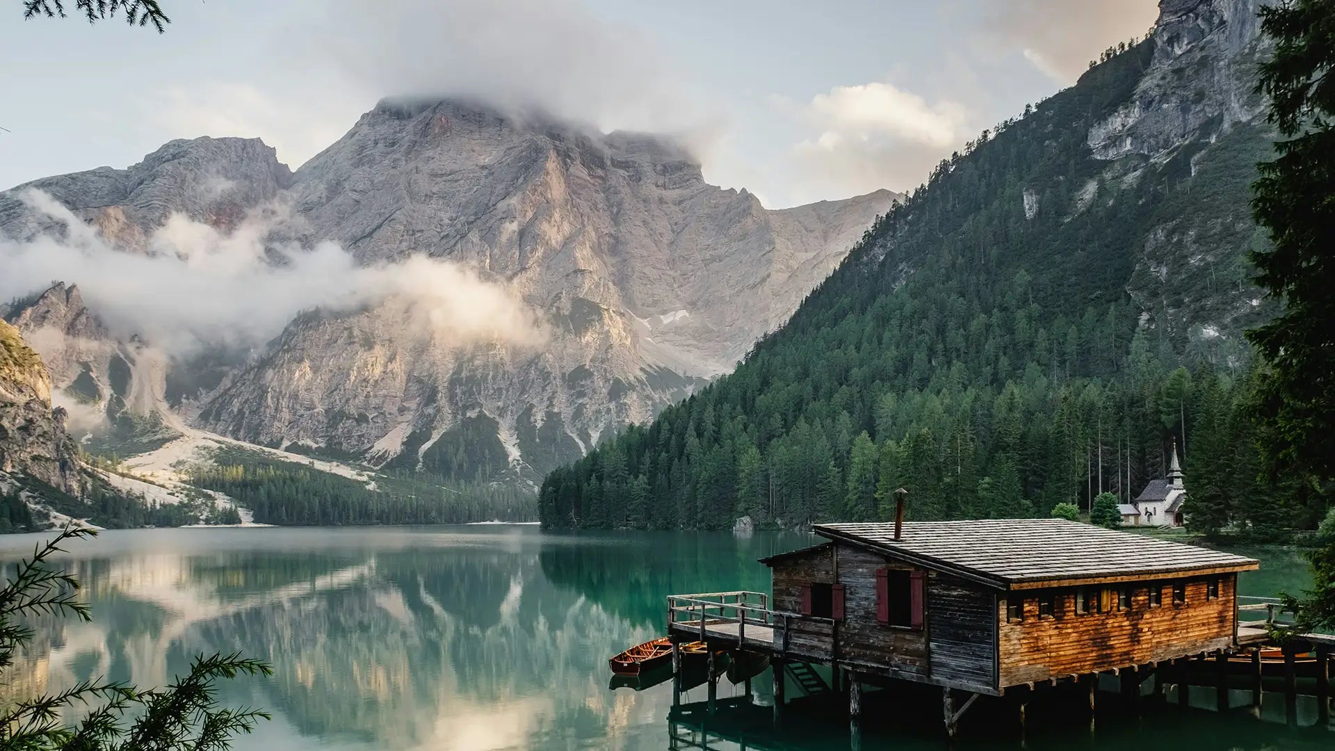 Idyllic view of a serene alpine lake reflecting towering mountains, featuring a rustic wooden cabin on a dock surrounded by lush green forests, capturing the tranquil essence of nature's beauty.