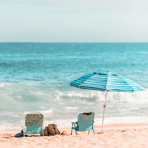 Two beach chairs and a blue striped umbrella set up on a sandy shore, facing the ocean on a clear, sunny day.