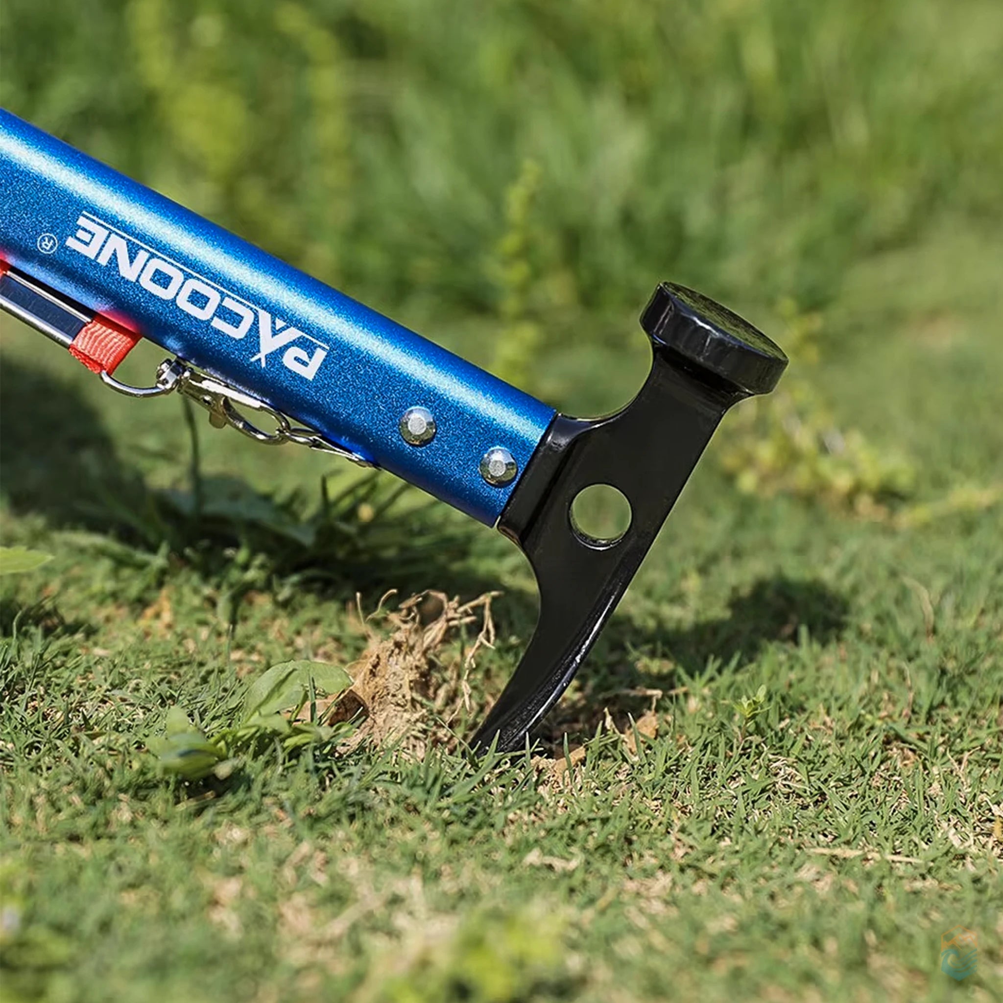 Close-up of blue Pacoone camping multi-tool hammer with black claw head prying into grassy terrain, showing rugged build and field-ready performance outdoors