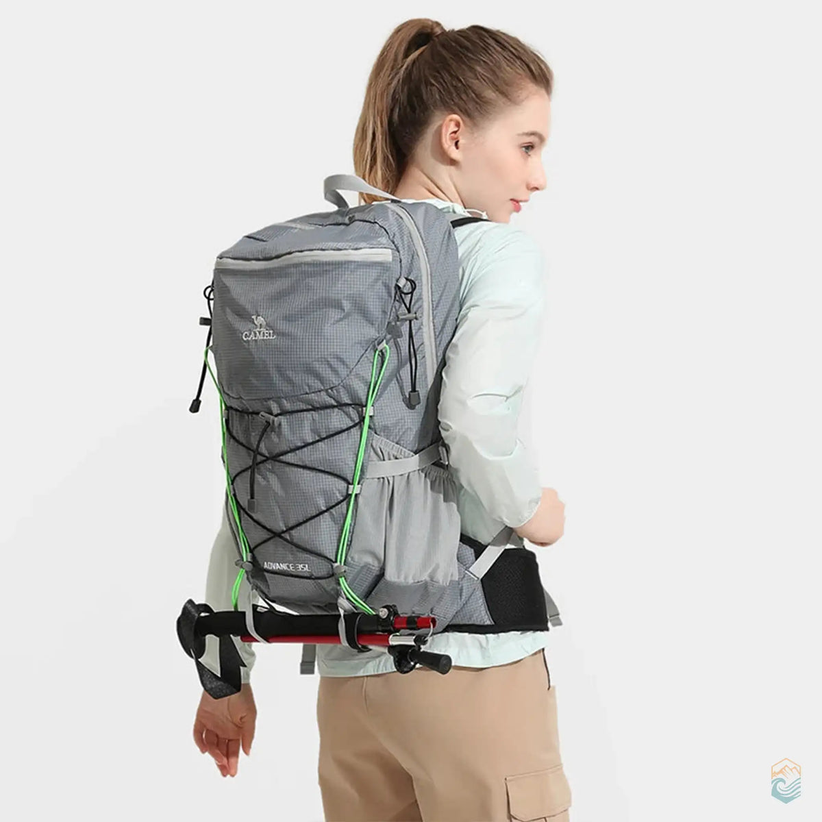 Woman wearing Camel outdoor backpack in gray, equipped with hiking poles, showcasing the backpack's practical design for outdoor trekking and adventure activities.