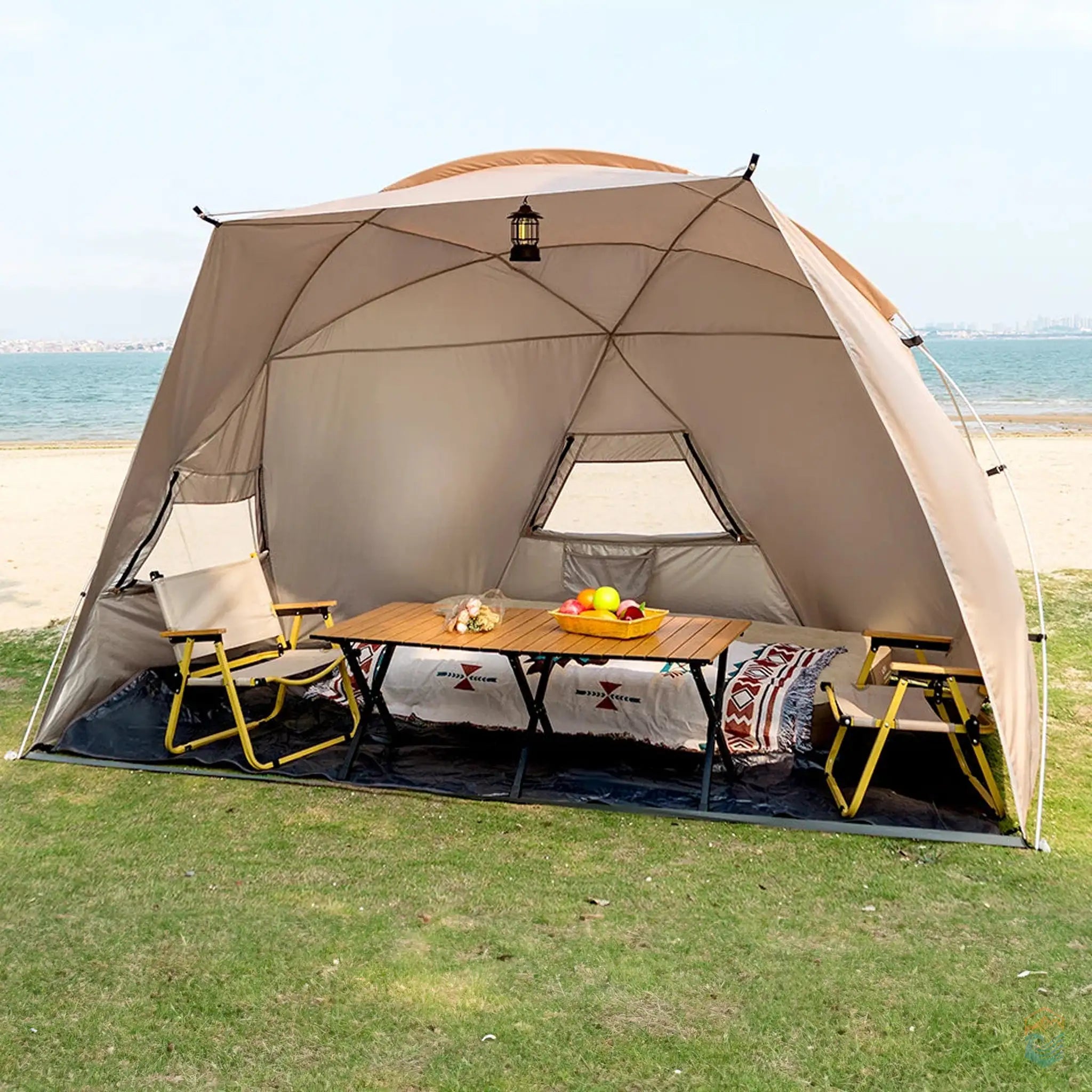 Khaki Sonuto beach shelter tent set up on a grassy area near the beach, featuring a spacious interior with room for 4-8 people. The tent is shown with aluminum poles, providing ample shade for outdoor dining and relaxation, perfect for beach outings or picnics.