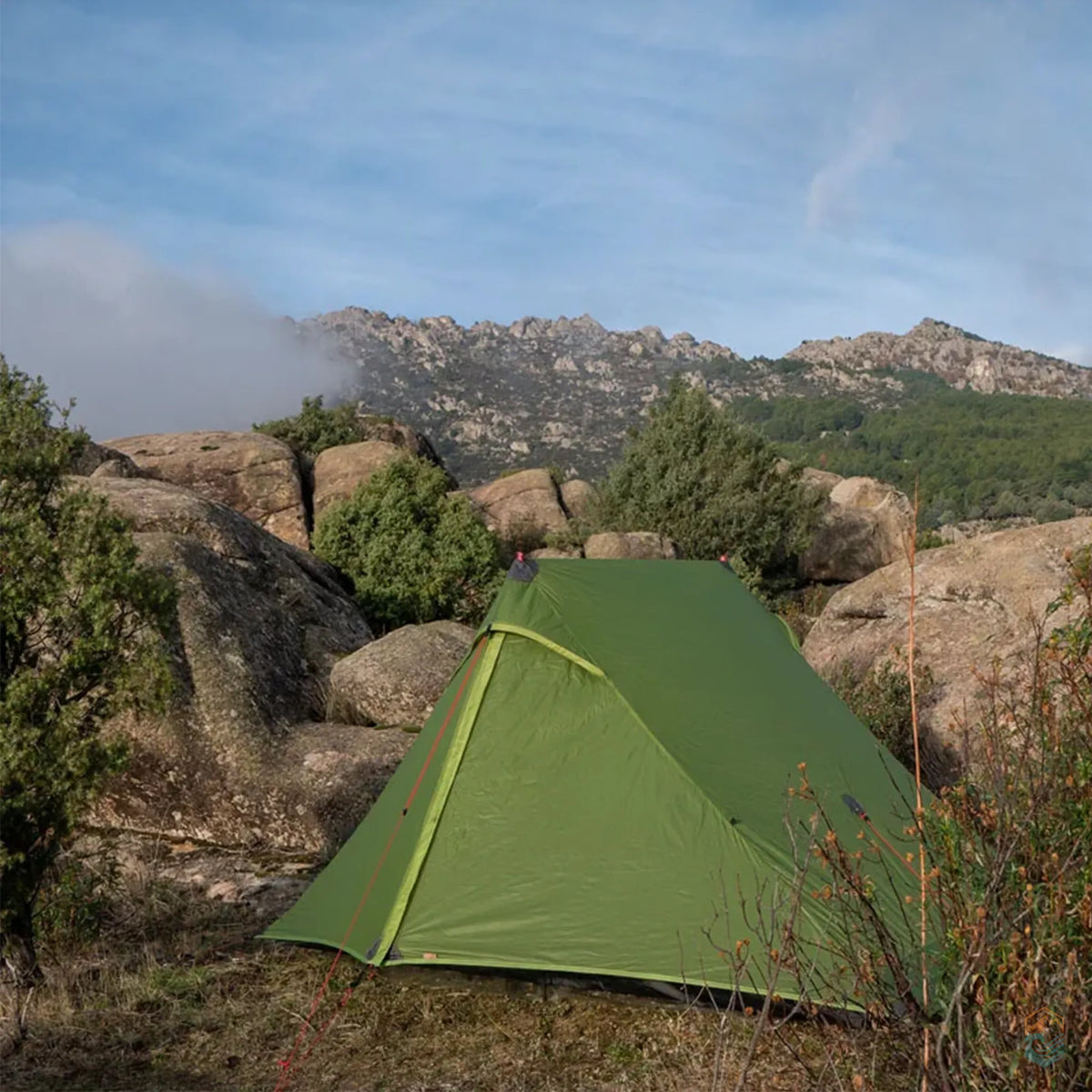 FLAME'S CREED Lanshan 2 Pro 4-season green tent set up in a rocky mountain landscape surrounded by boulders, shrubs, and distant peaks under a clear sky—ideal for rugged backcountry camping and backpacking in remote terrain