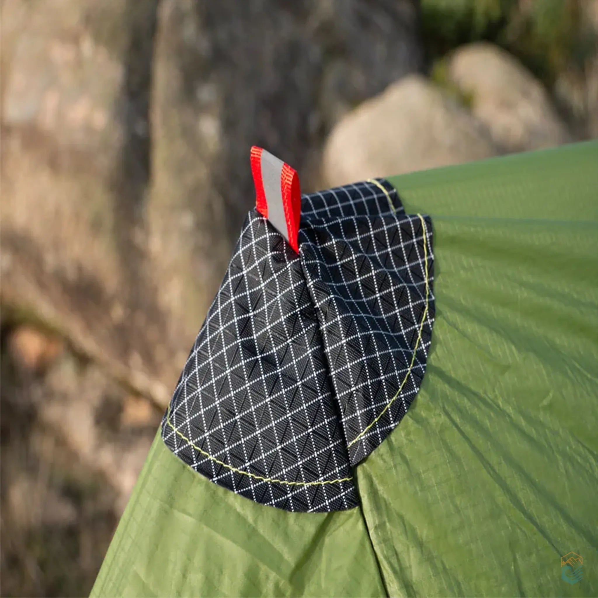 Close-up of FLAME'S CREED Lanshan 2 Pro green tent showing reinforced triangular tip with red pull loop and grid-stitched black patch, designed for securing trekking pole setup and increasing durability in rugged camping environments.