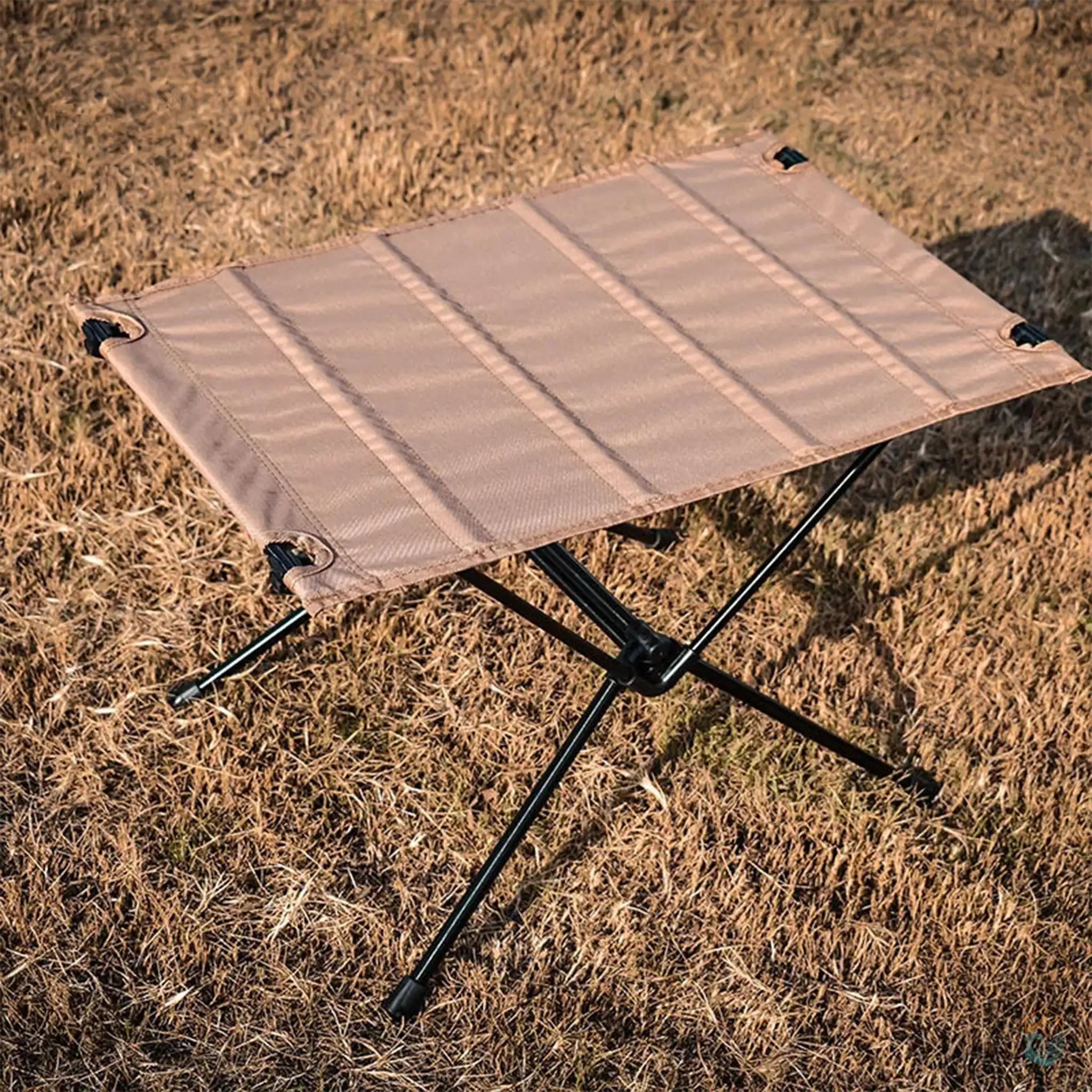 Sand-colored collapsible camping table with an aluminum frame, set up on dry grass, ideal for portable and lightweight outdoor activities.