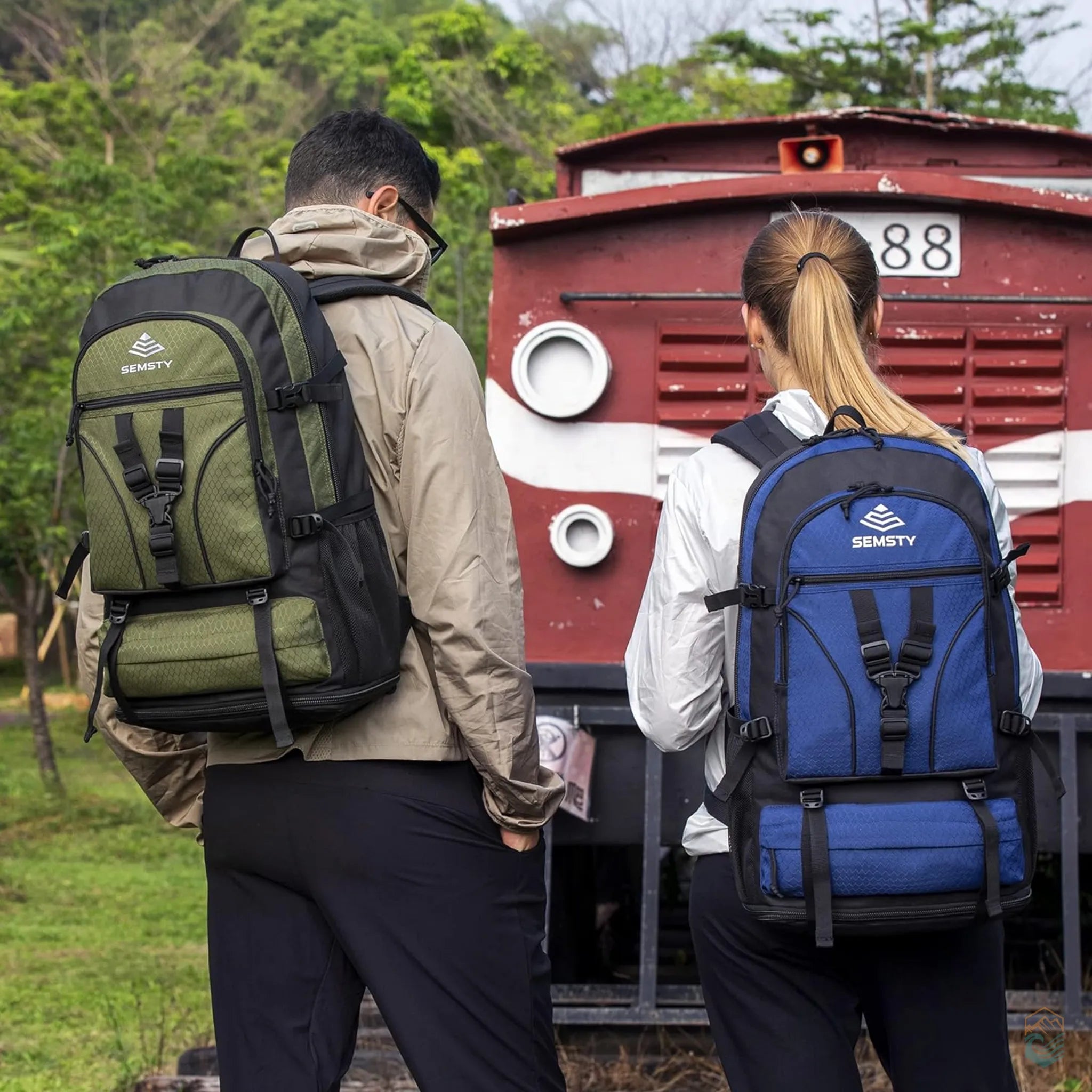Two hikers wearing Semsty expandable hiking backpacks—one in green and one in blue—standing in front of a vintage red train, showcasing the ergonomic design and comfort of the backpacks during outdoor travel and day hikes.