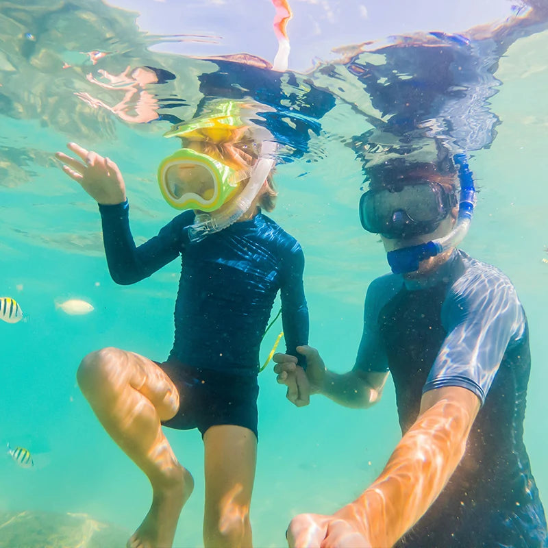 Two people snorkeling underwater, surrounded by colorful tropical fish, wearing snorkel masks and swimwear.