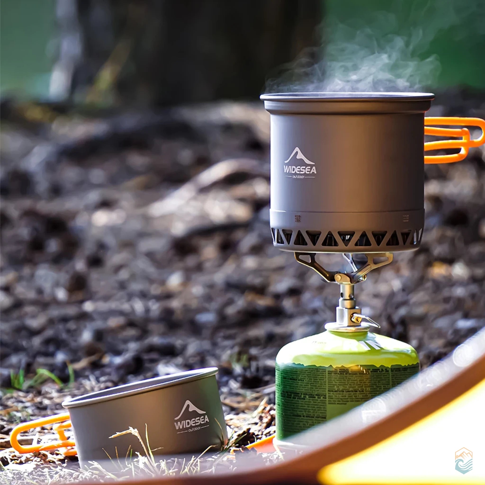 Widesea camping cookware pot heating over a portable gas stove in the outdoors with steam rising, while a second pot rests nearby on the forest ground, showing active use and rugged performance