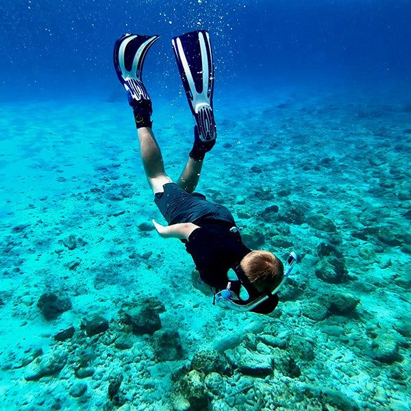 Young kid diving in crystal clear blue water, snorkeling with fins and exploring the underwater world.