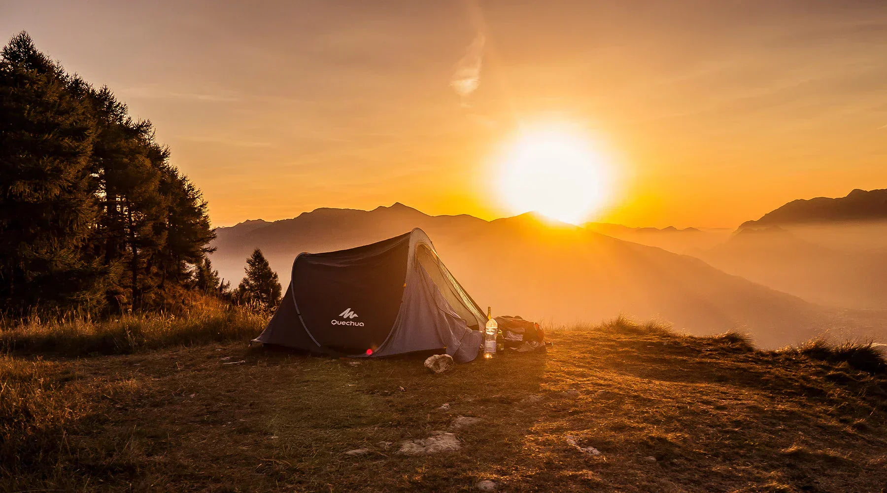 Solo camping tent pitched on a grassy mountain ridge at sunrise with pine trees on the left and a golden sun rising over misty peaks in the background, capturing the peaceful beauty of a beginner’s first camping experience.