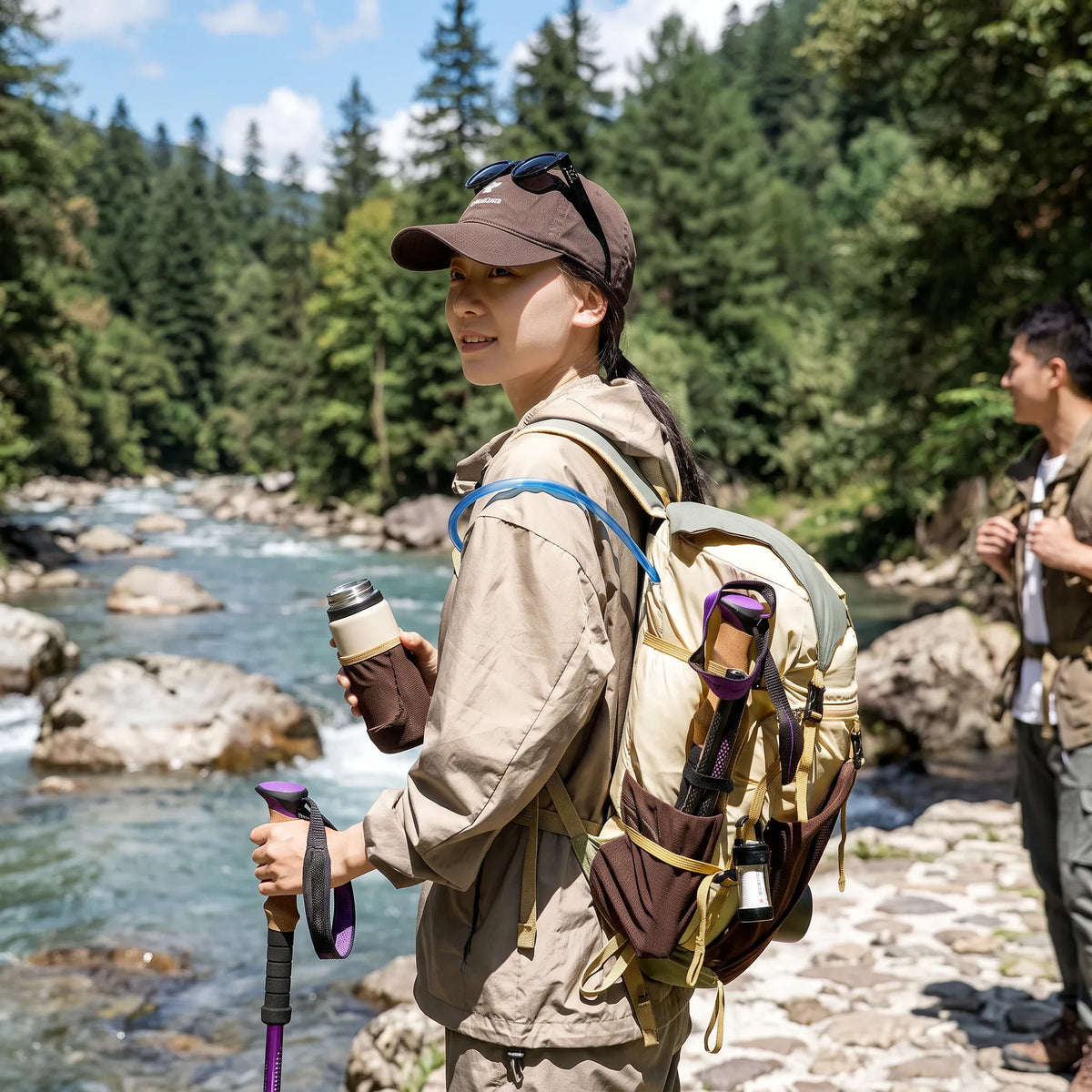 Woman wearing a BISINNA 22L hiking backpack with trekking poles and hydration gear beside a mountain river.