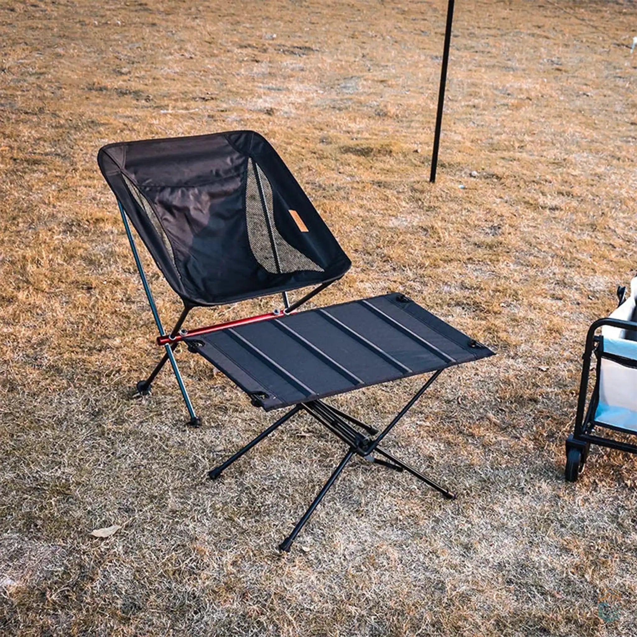 Black collapsible camping table paired with a matching camping chair, set up on dry grass during an outdoor activity, ideal for lightweight and portable camping setups.