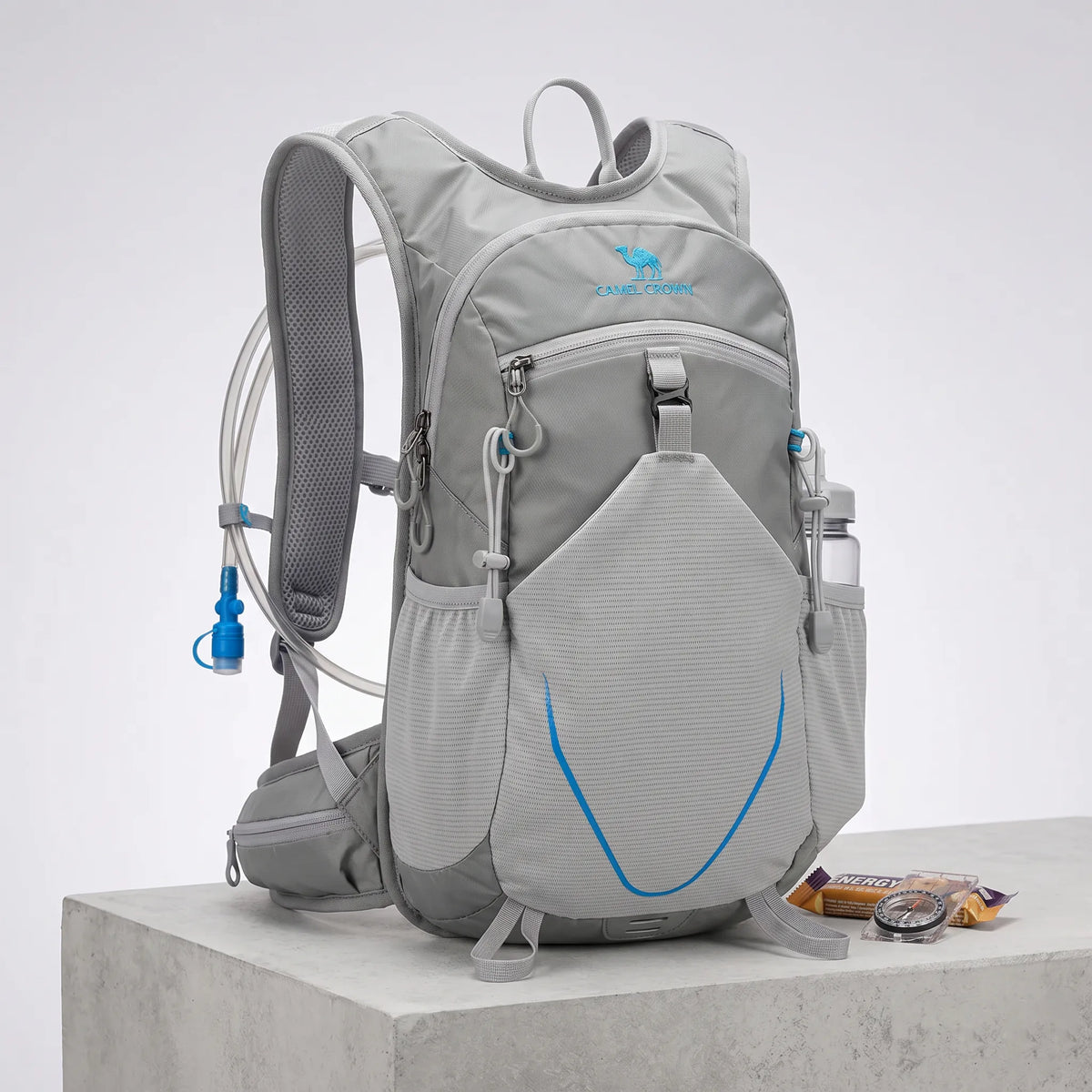 Camel 12L hiking backpack in gray with hydration reservoir tube, lightweight waterproof construction, breathable shoulder straps, front mesh storage pocket, and compact 12L capacity for hiking, trekking, camping, cycling, trail running, and outdoor travel.