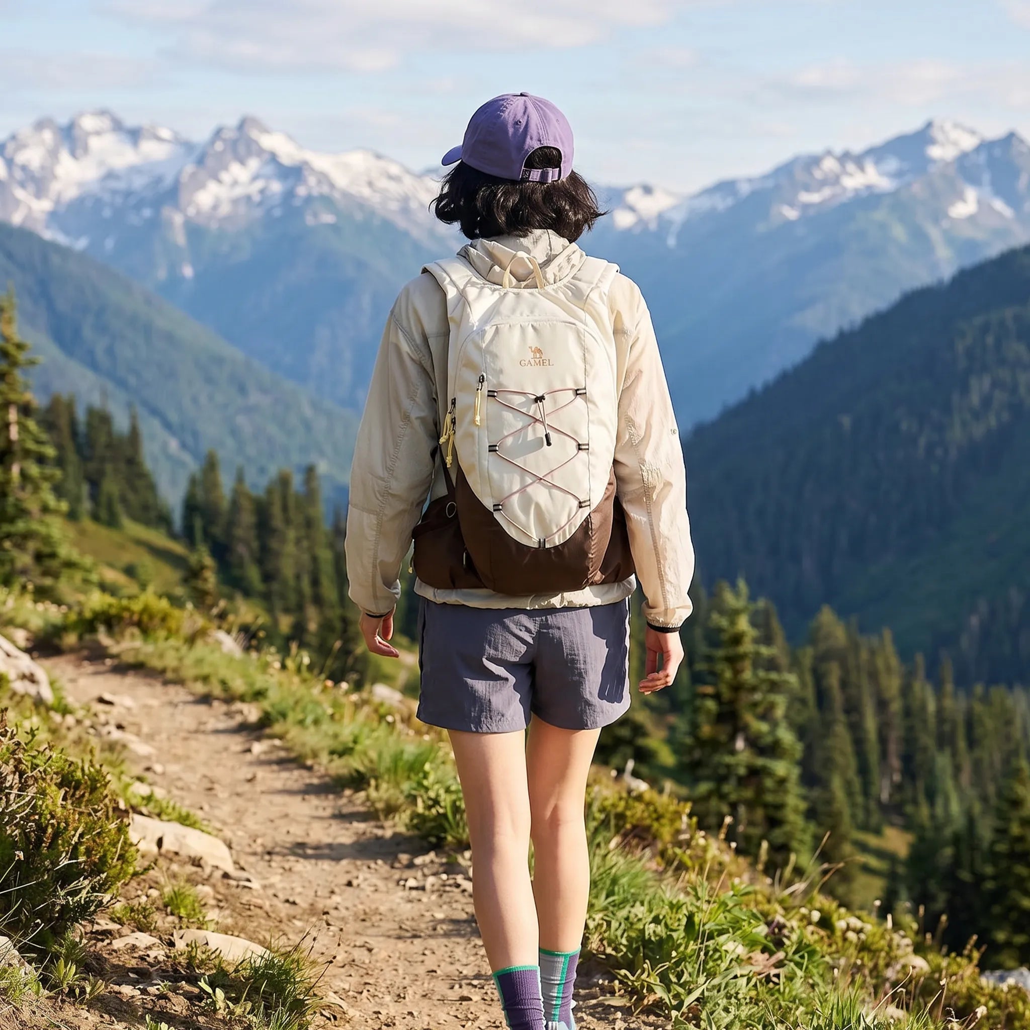 Hiker wearing a brown Camel 20L lightweight hiking backpack while walking along a mountain trail with snow-covered peaks.