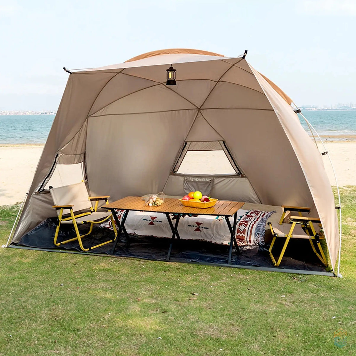 Khaki Sonuto beach shelter tent set up on a grassy area near the beach, featuring a spacious interior with room for 4-8 people. The tent is shown with aluminum poles, providing ample shade for outdoor dining and relaxation, perfect for beach outings or picnics.