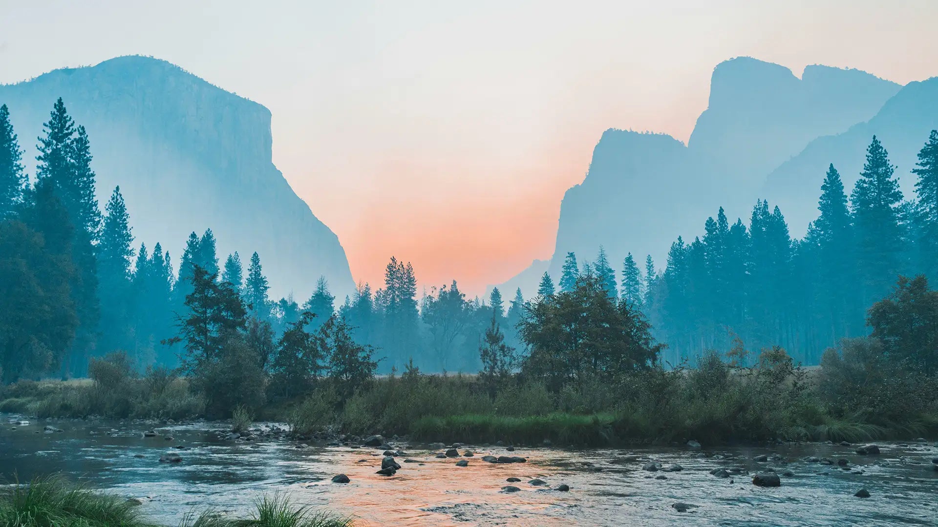 Misty sunset over a serene river flowing through a valley with towering cliffs and dense forest. The golden hues of the sunset cast a warm glow on the water, creating a peaceful and picturesque scene in the wilderness. The atmosphere is tranquil, perfect for nature lovers and outdoor enthusiasts seeking solace in a scenic landscape.