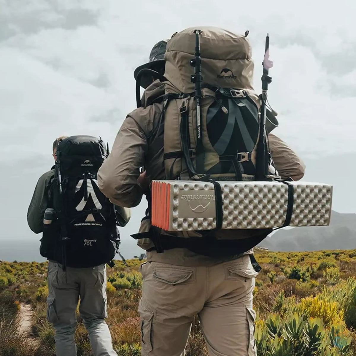 Two hikers wearing Naturehike 70L camping backpacks trekking through a scenic outdoor landscape, demonstrating the pack's capacity and ergonomic design.