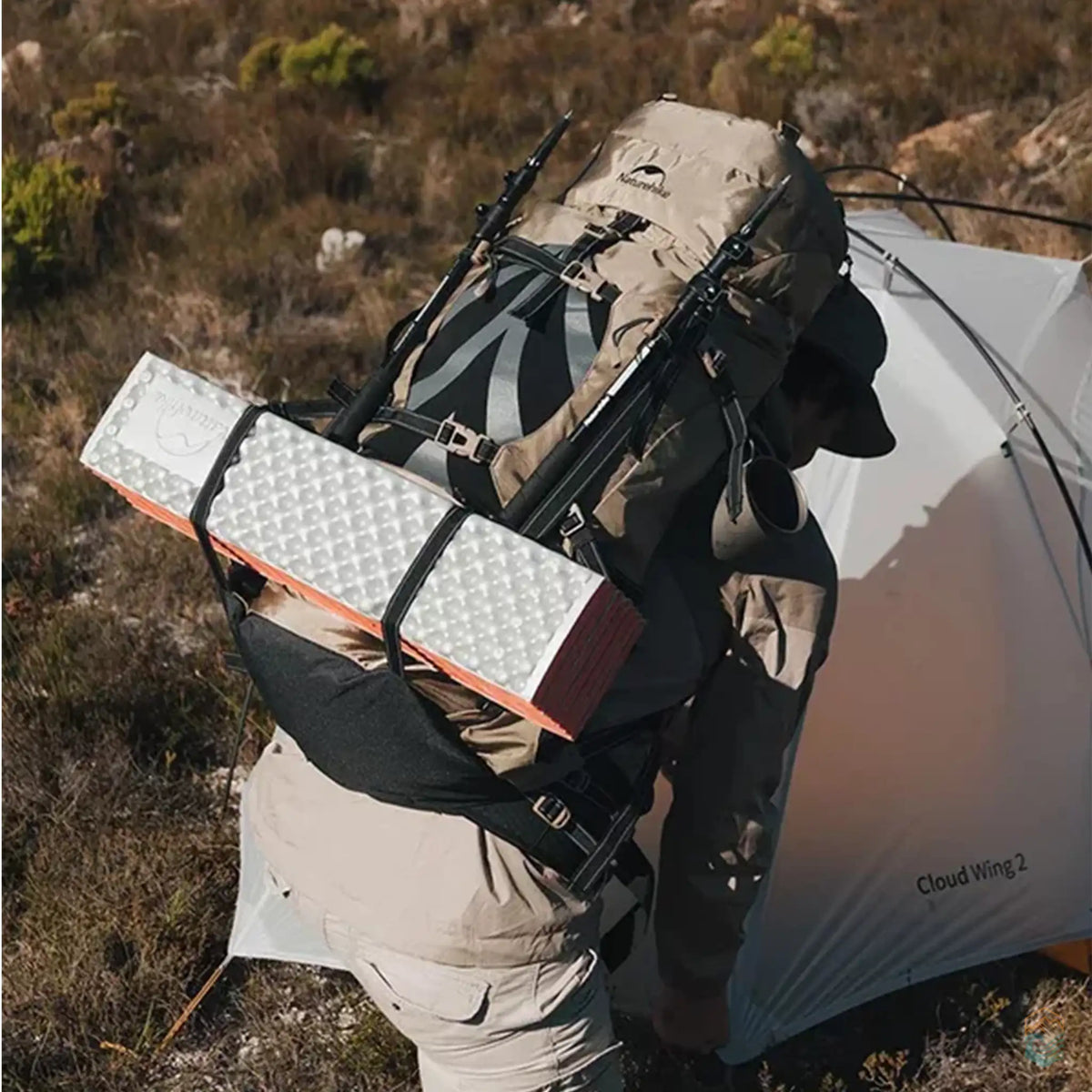 Camper kneeling beside a tent while wearing a Naturehike 70L camping backpack, preparing to set up camp in a rugged outdoor environment.