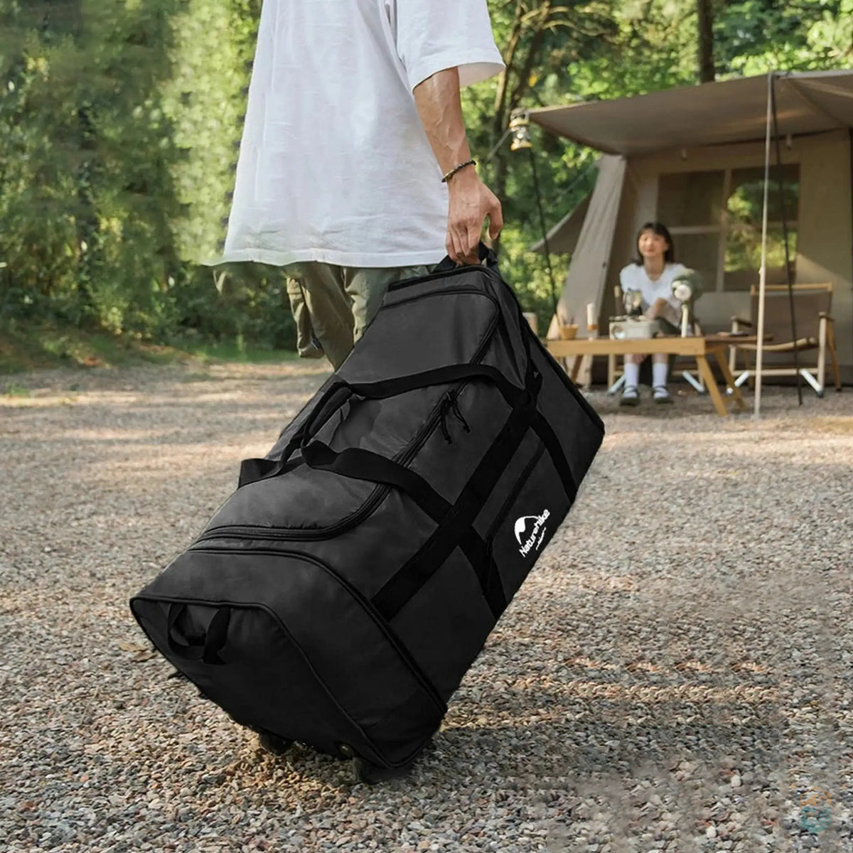 Person carrying a black Naturehike 88L large capacity camping duffel bag with wheels outdoors, showcasing its portability and durability in a camping setting. The inset highlights the bag's sturdy wheels for easy transport on rough terrain.