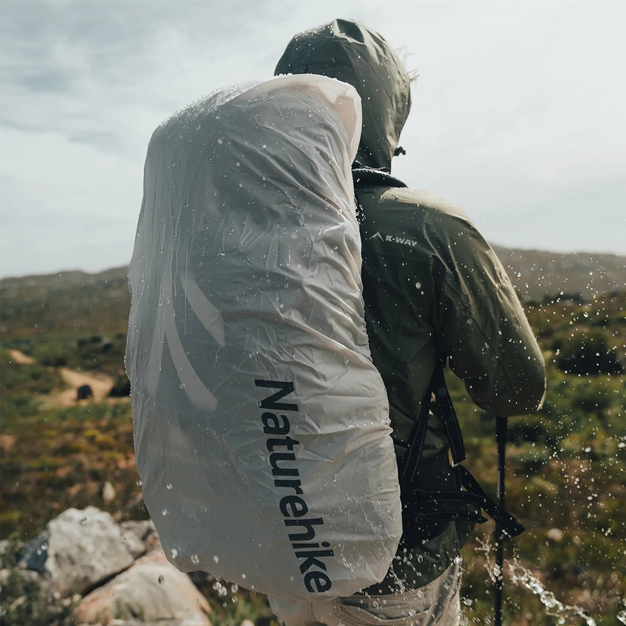 Hiker wearing the Naturehike Discovery 70L backpack protected by the included waterproof rain cover during wet outdoor conditions.