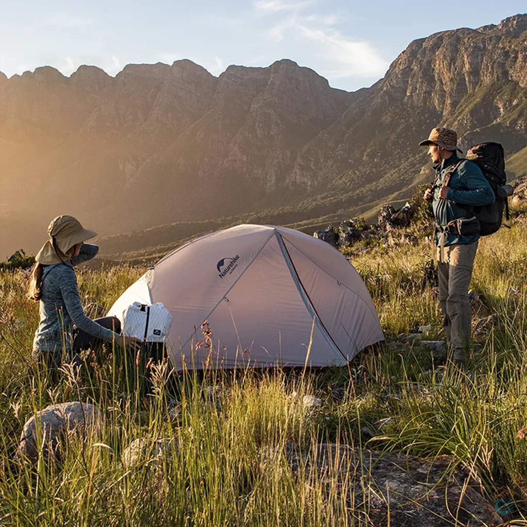 Two hikers setting up a Naturehike Star River 2-person gray tent in a scenic mountain valley during golden hour, surrounded by grass and rugged terrain