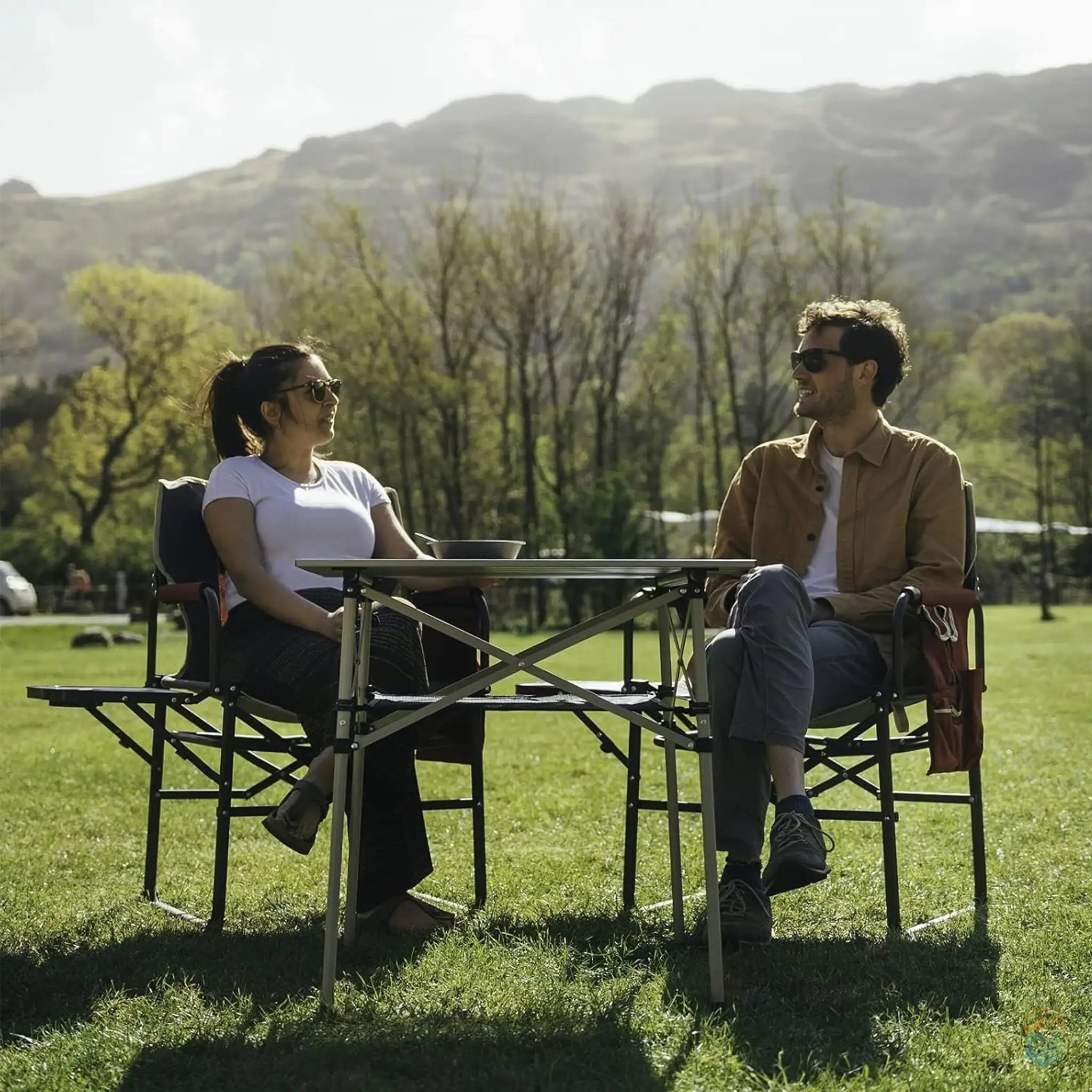 Two people sitting in SunnyFeel folding camping director's chairs with side tables, enjoying a scenic outdoor setting.