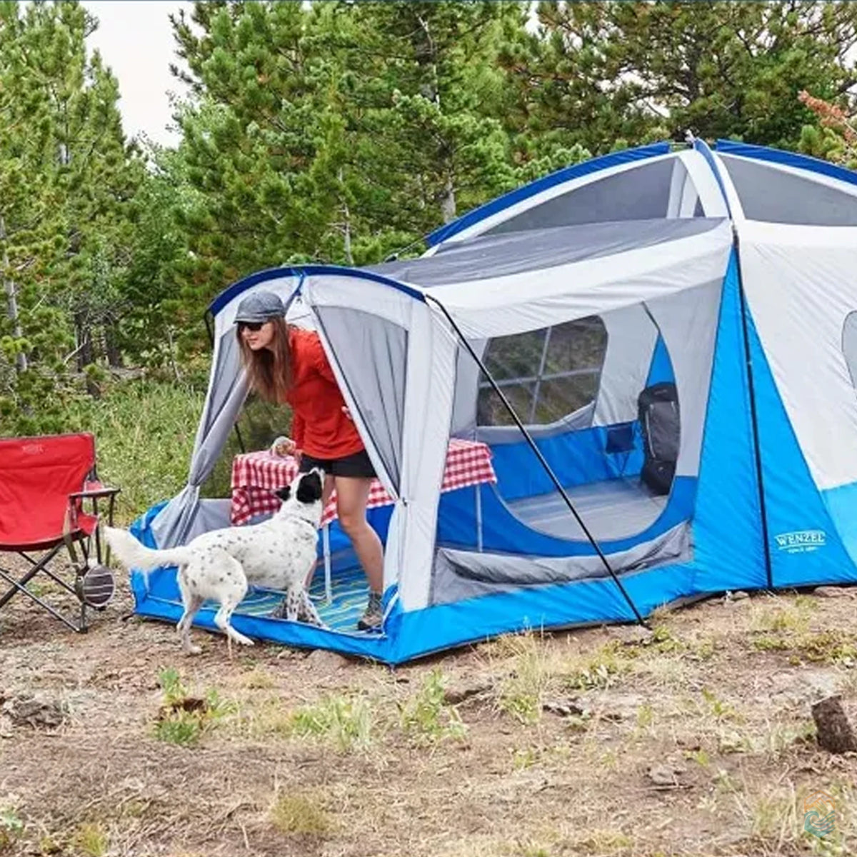 Woman stepping out of the Wenzel Klondike tent's screen room to greet her dog during a forest camping trip