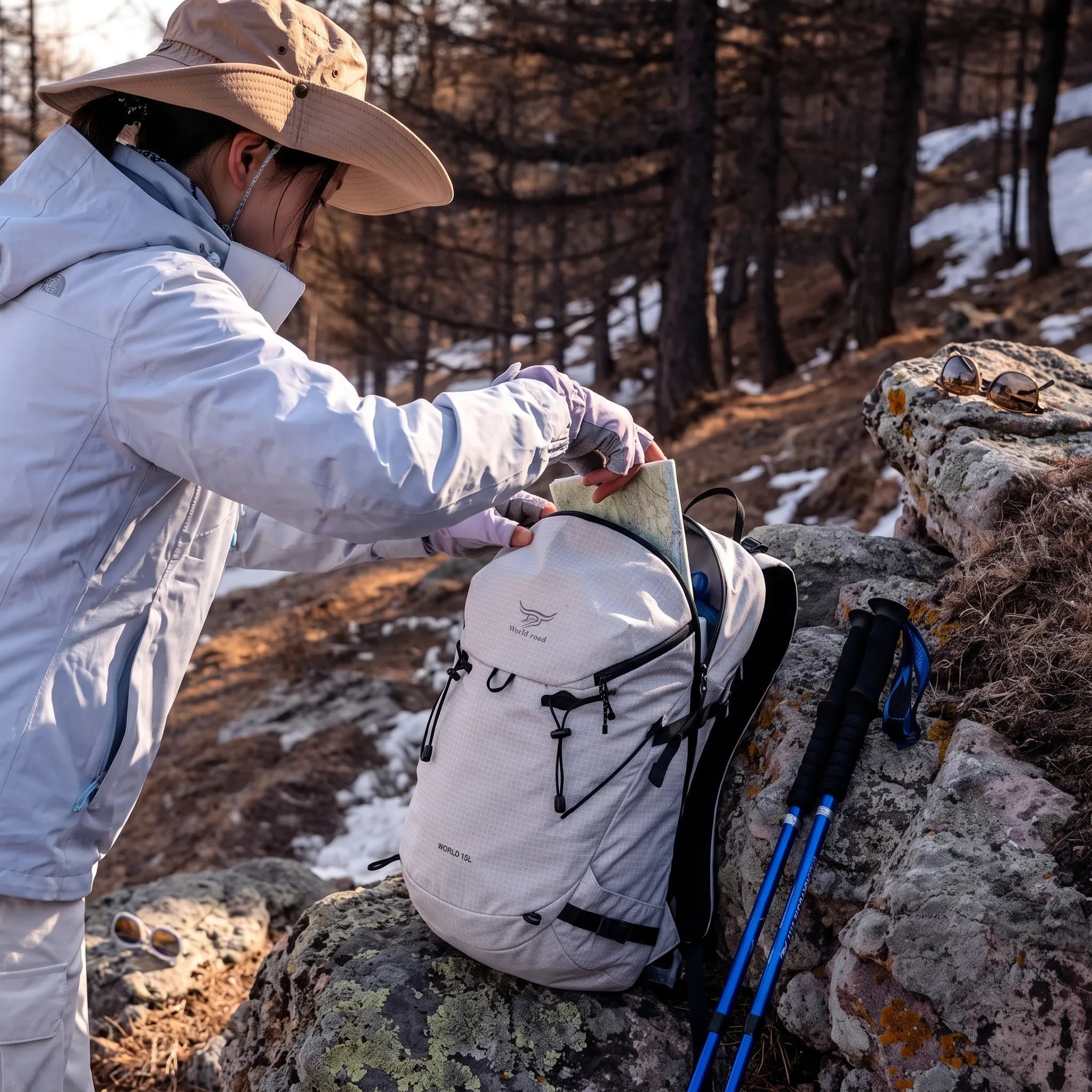 Hiker using the white World Road 15L Urban Outdoor Hiking Backpack while retrieving a trail map during a mountain hike.